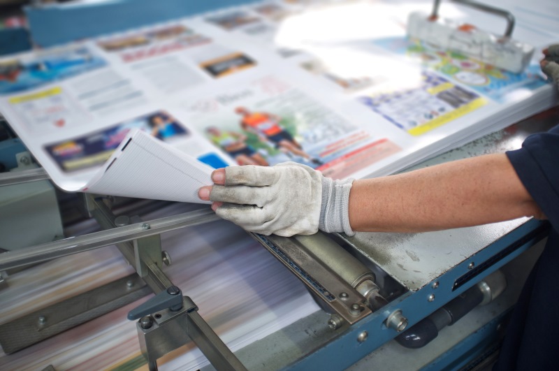 Gloved hands shuffling through magazine pages on an industrial printer