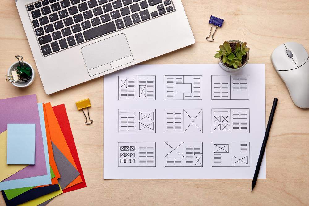 A layout design sheet on a wooden desk in front of an open laptop
